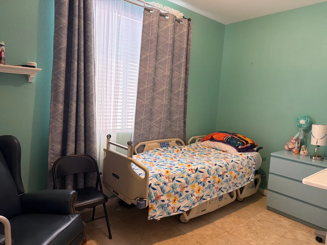 A resident room at Caring Angels Henderson with a care bed, recliner, and curtained window