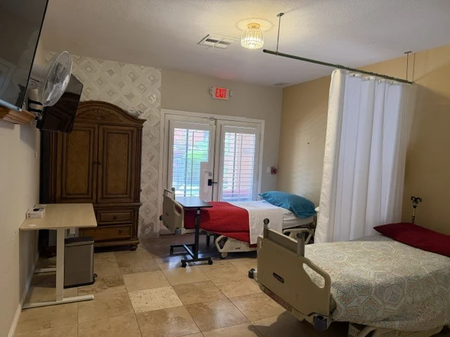 A comfortable resident room with twin beds, a wood armoire, and French doors at Caring Angels Henderson